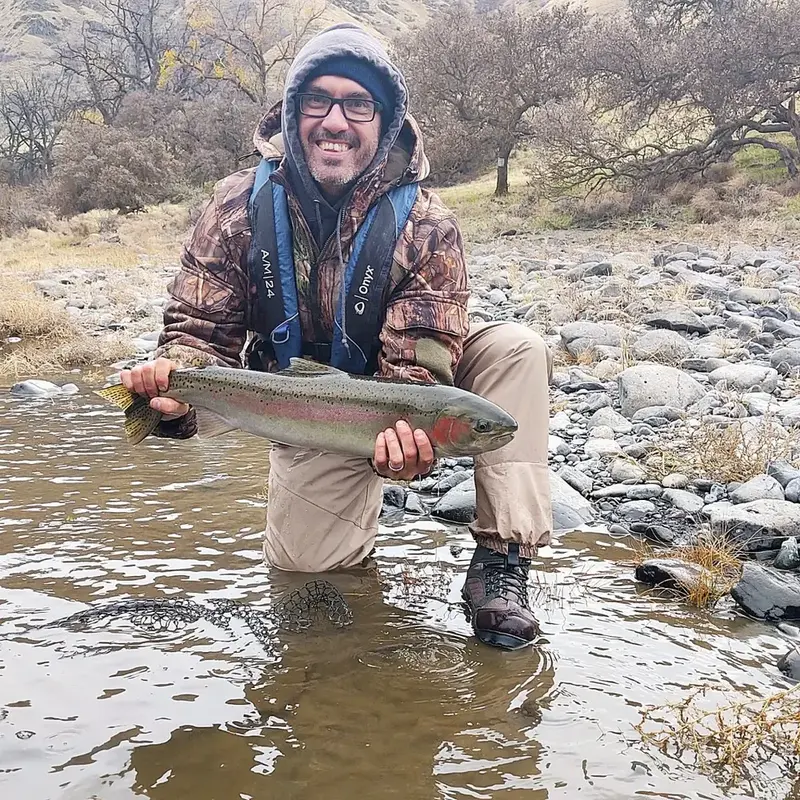 J.C. kneeling in the river with a steelhead